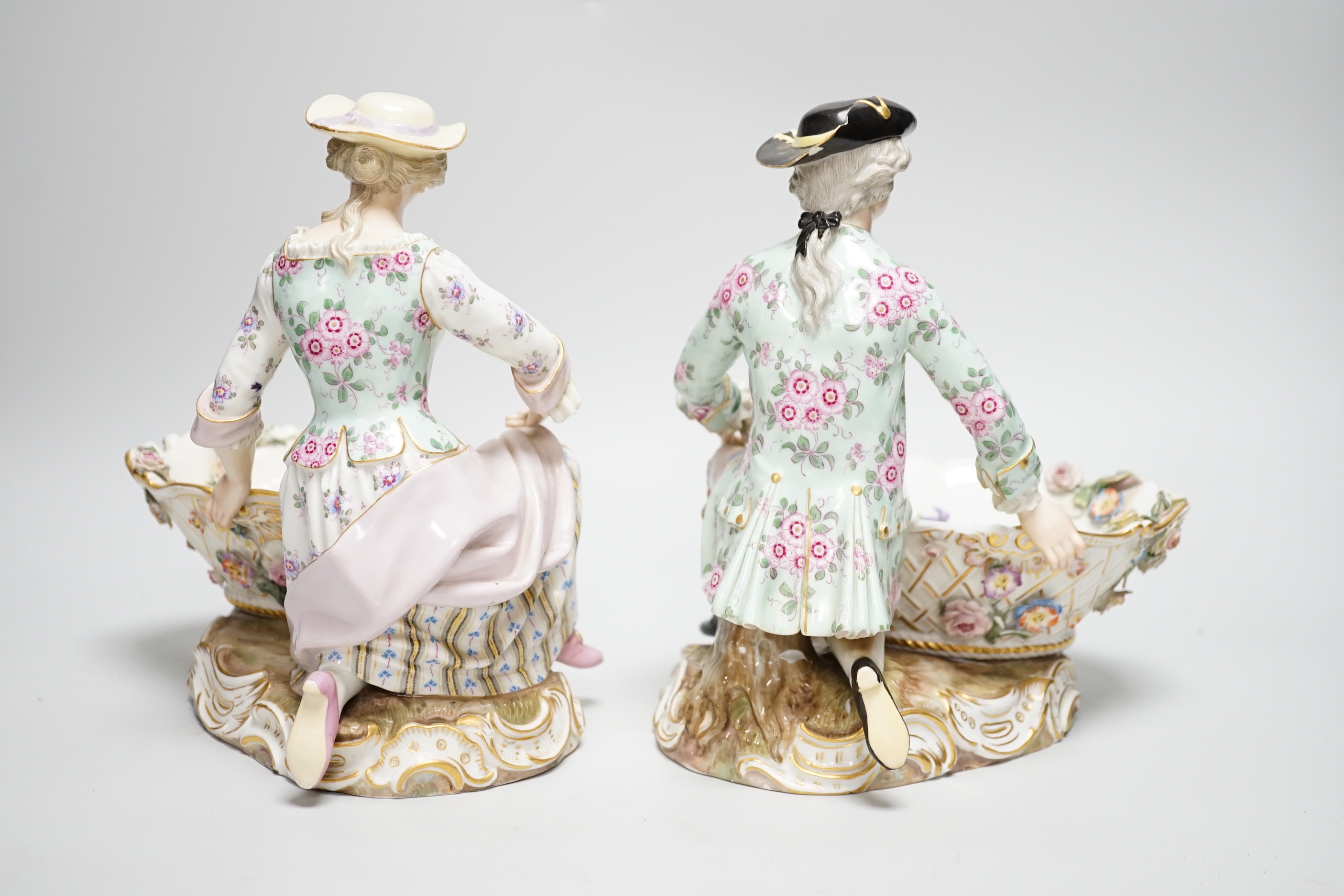 A large pair of Meissen salts in the form of a seated man and a woman in 18th century dress (a.f.), 21cm high